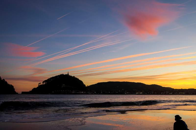 Un hombre observa el amanecer en la playa de Ondarreta de San Sebastián.