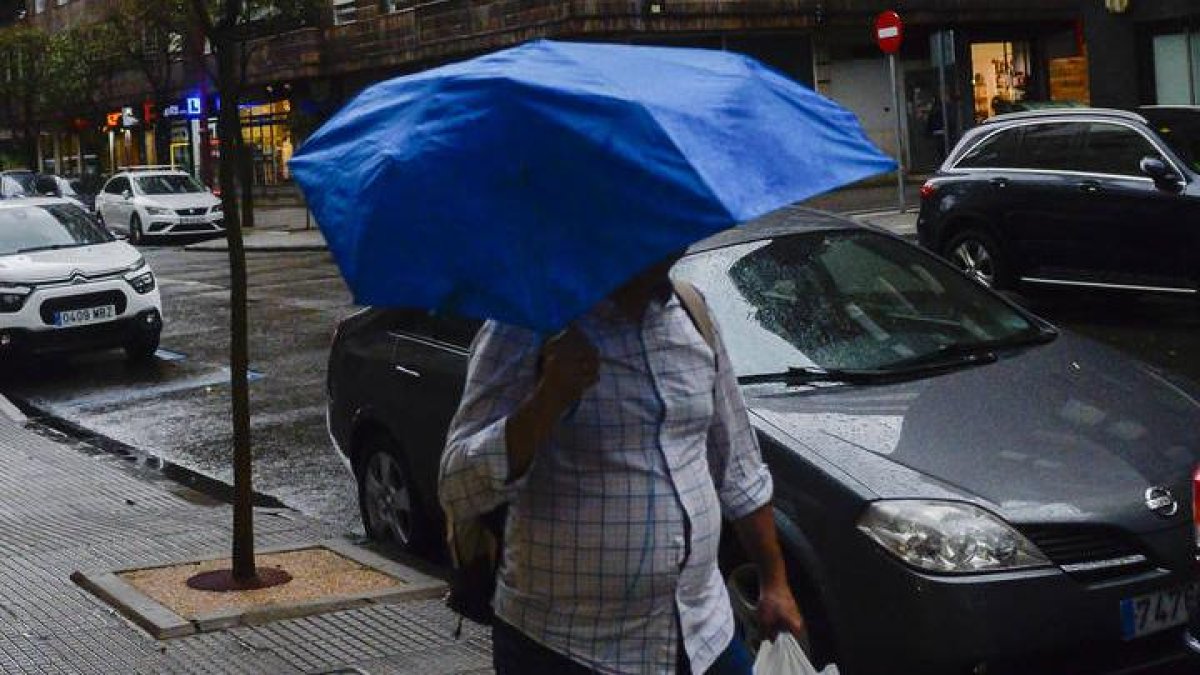 Un hombre pasea por León en un día de lluvia y viento
