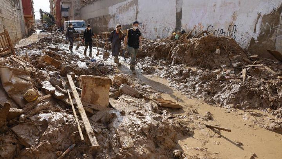 Voluntarios pasan ante los escombros acumulados a los lados de una calle de Masanasa, Valencia, este jueves.