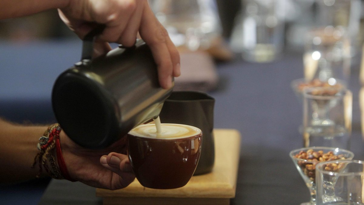 Un camarero sirve un café con leche en un bar.