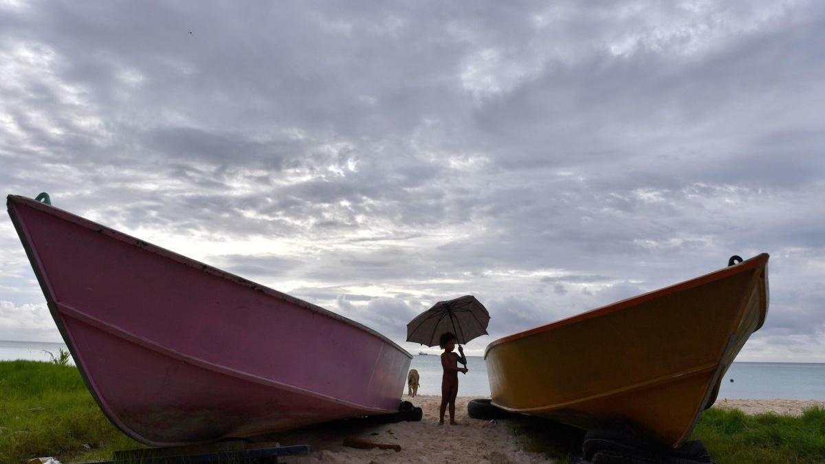 Un niño sujeta un paraguas roto frente al lago de Funafutio. MICK TSIKAS