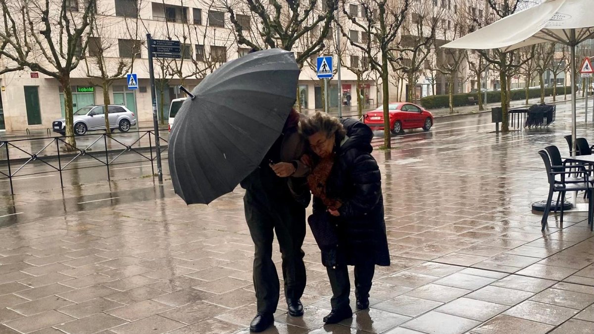 Dos personas caminan por la calle en León en pleno temporal de lluvia y viento