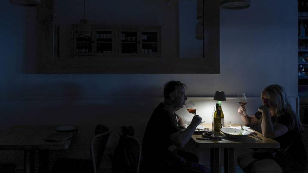 Una pareja cena a la luz de una lámpara recargable en la noche del apagón.