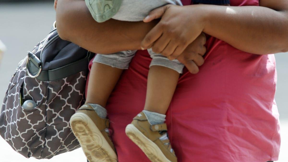 Una mujer sostiene a un bebé en brazos mientras pasea por la calle.