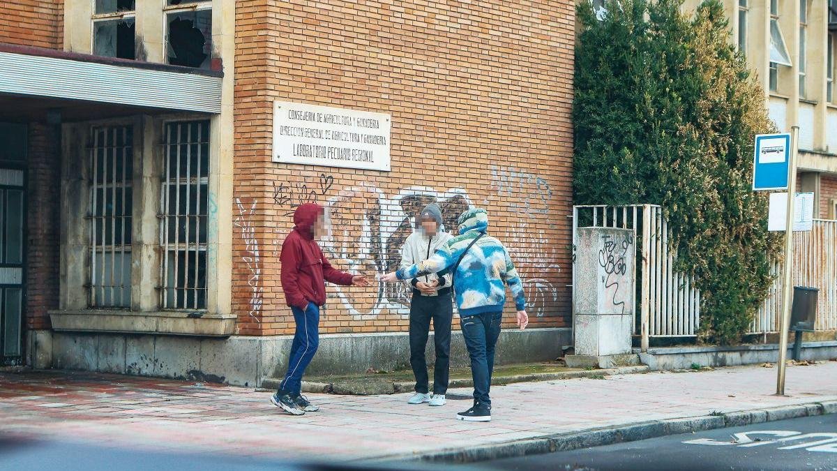 Tres individuos realizan una transacción a plena luz del día, a las puertas de la entrada principal del edificio.
