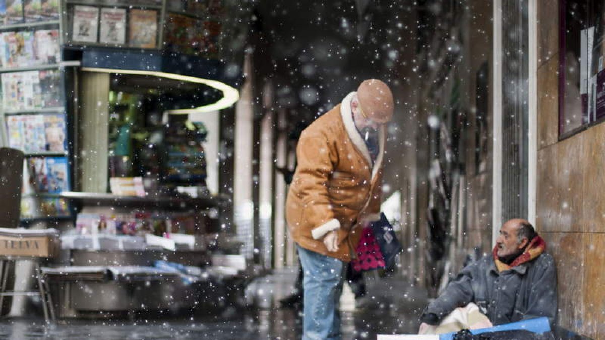 Un hombre recibe una limosna en medio de la tormenta de nieve en Huesca.