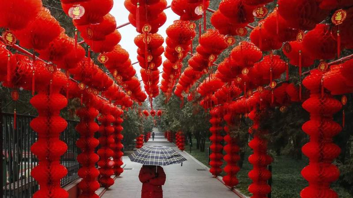 Una mujer pasea bajo la lluvia y entre las características lamparillas rojas en el popular parque Ditan, en Pekín. ROMAN PILYPEY