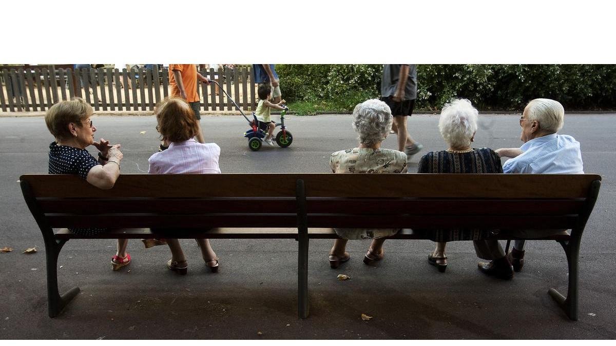 Un grupo de ancianos descansan en un banco en un parque de Barcelona. /