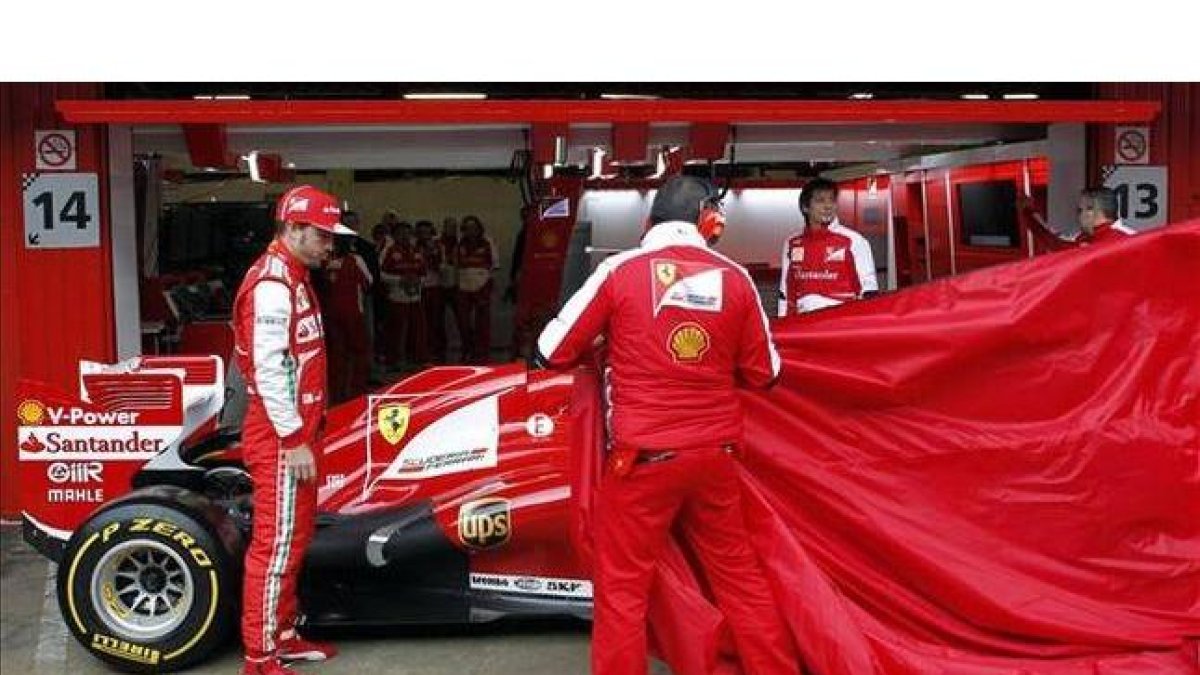 Alonso mira cómo los mecánicos destapan su Ferrari, en Montmeló.