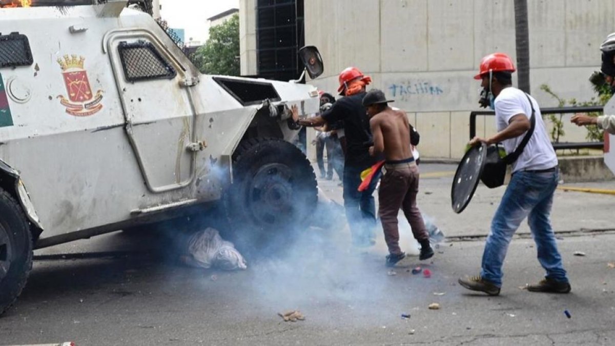 Un manifestante yace bajo una tanqueta policial en Caracas.