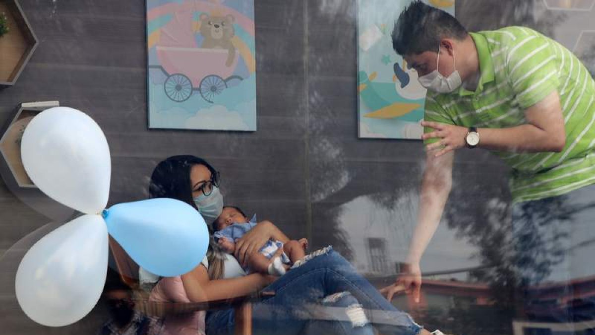 Una joven pareja muestra a su hijo a la familia en Monterrey a través de un cristal por el covid. MARÍA JULIA CASTAÑEDA