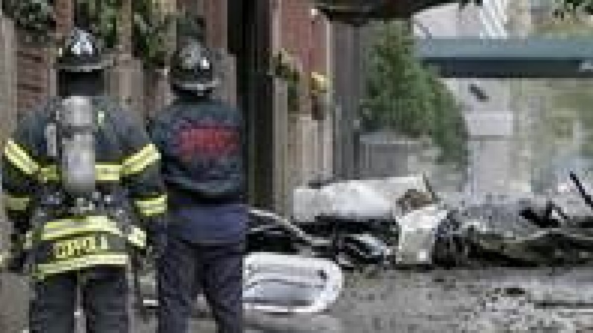 Dos bomberos observan los restos de la aeronave que se estrelló contra un inmueble en Nueva York