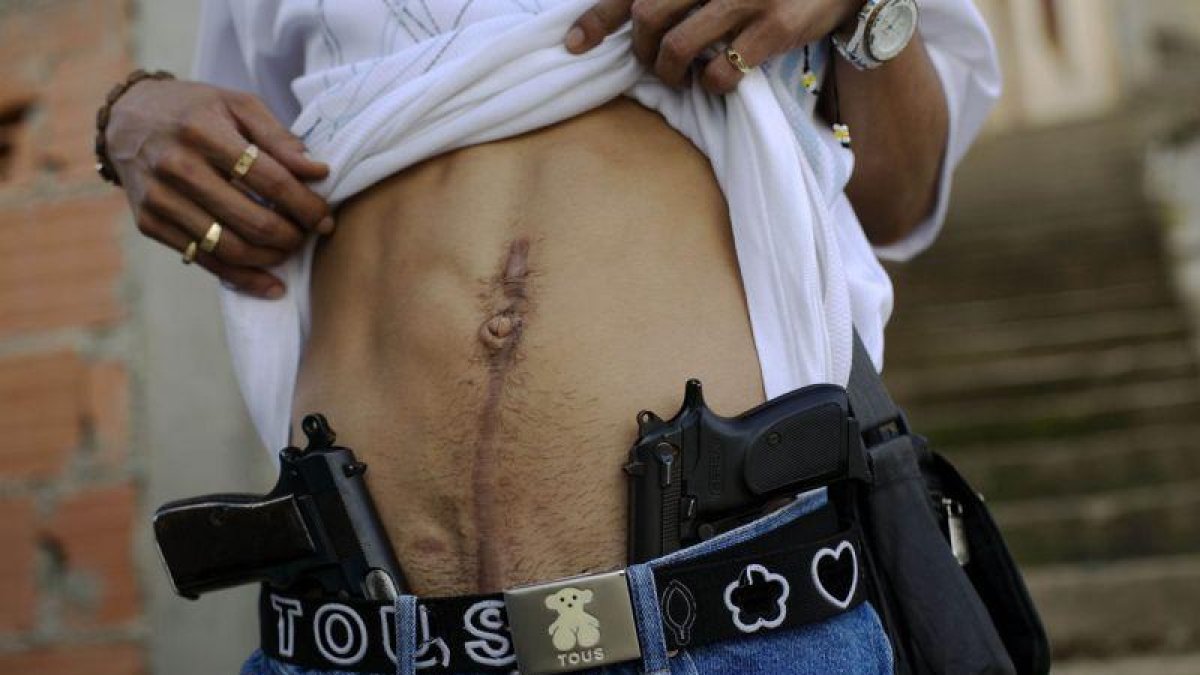 Un traficante de drogas muestra su herida de bala y su arma en Caracas.