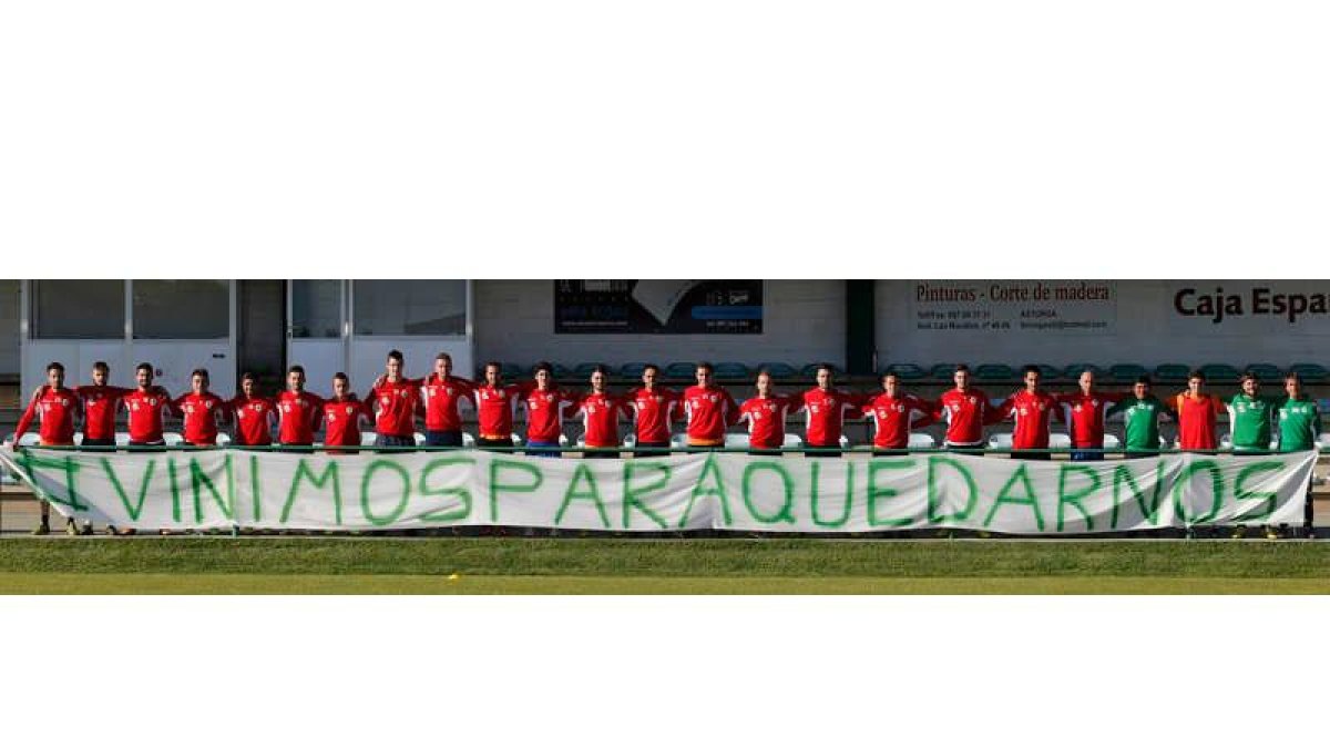 Jugadores y cuerpo técnico del Astorga posan detrás de una pancarta en la que se lee ‘Vinimos para quedarnos’, deseo que espera cumplir el domingo el plantel verde