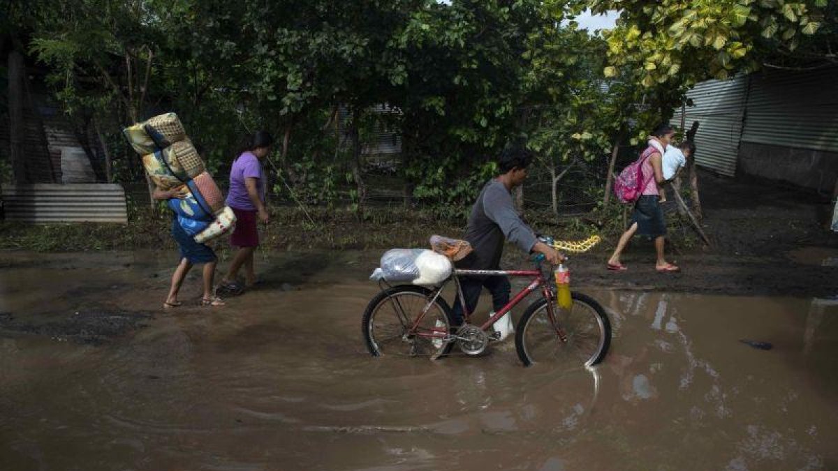Varias personas caminan con frazadas y provision por una calle inundada despues que un cauce se desbordara en el municipio de Tipitapa.