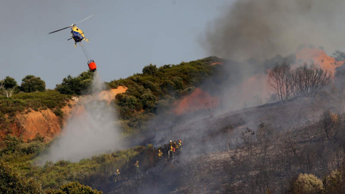Un helicóptero ataca las llamas desde el cielo mientras las brigadas trabajan en tierra. BARREDO