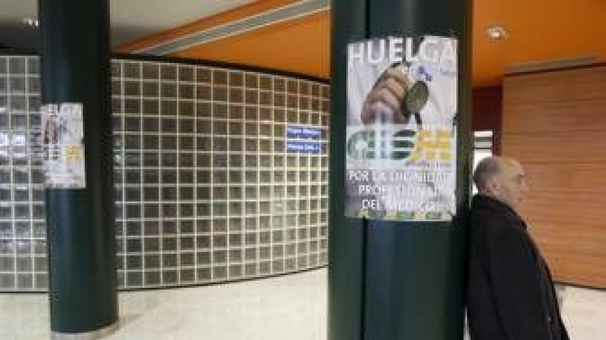 Un paciente espera apoyado en una columna con el cartel de la huelga