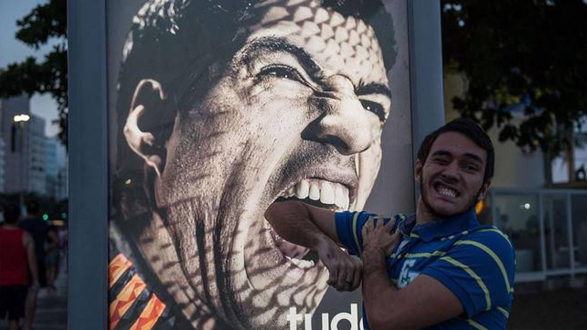 Un aficionado bromea ante un cartel publicitario protagonizado por Luis Suárez, en Copacabana.