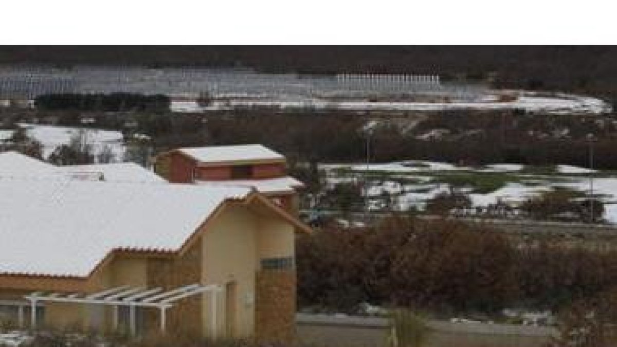 Varias viviendas y, al fondo, las placas fotovoltaicas del huerto solar.