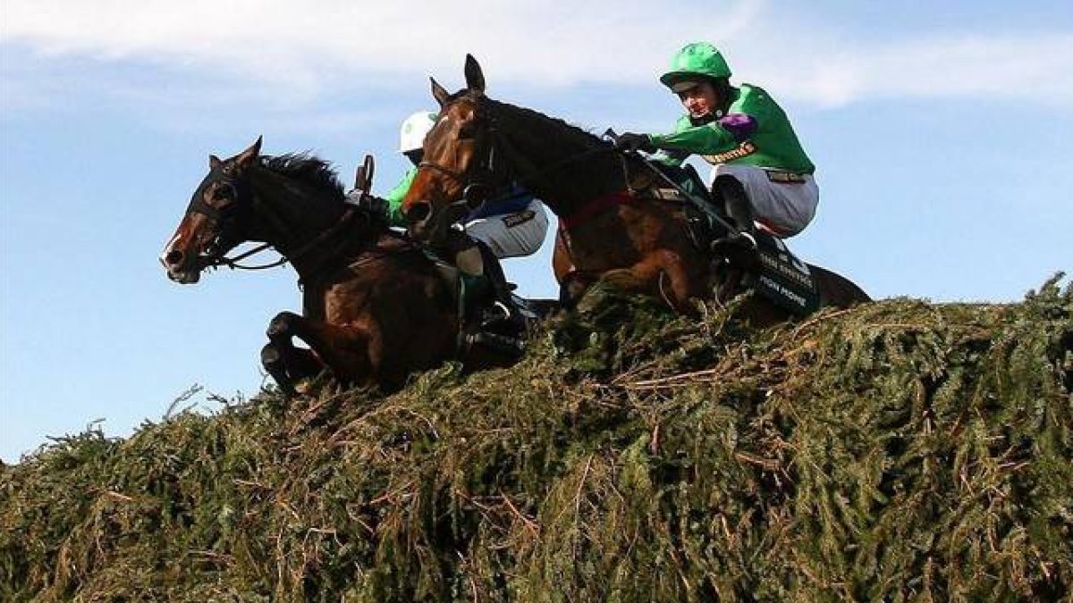 Dos caballos con sus respectivos jinetes saltan un obstáculo en el Grand National de Aintree, en el 2009.