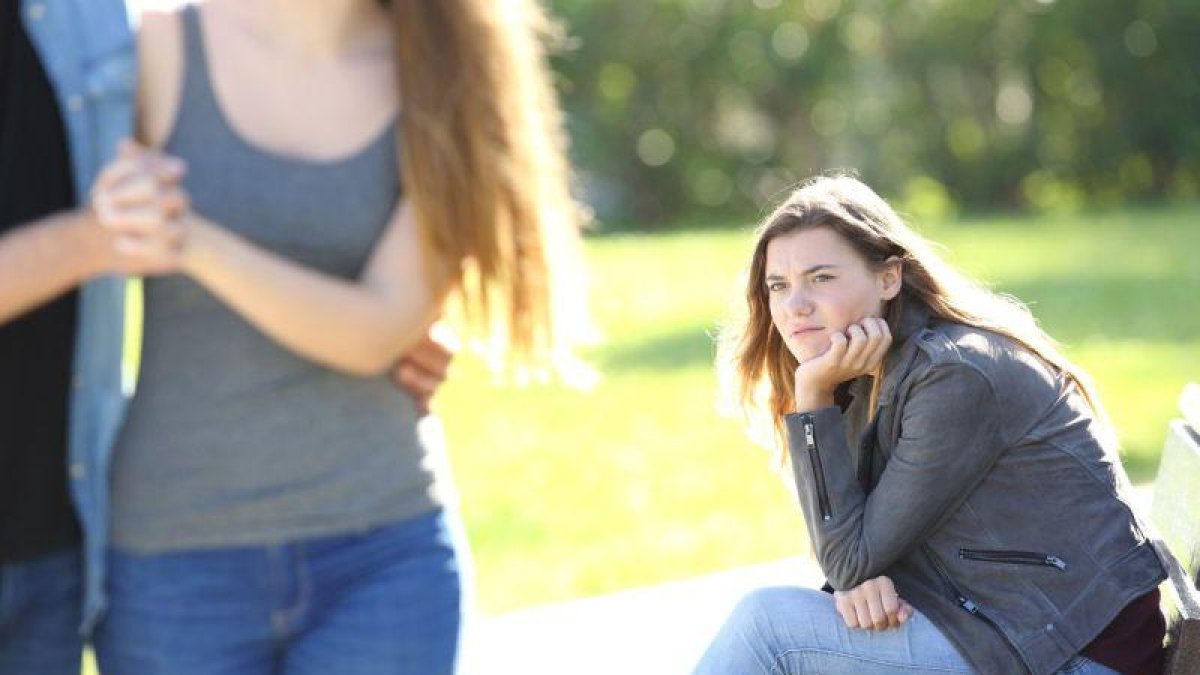 Una chica sentada en el parque siente envidia al ver a una pareja.