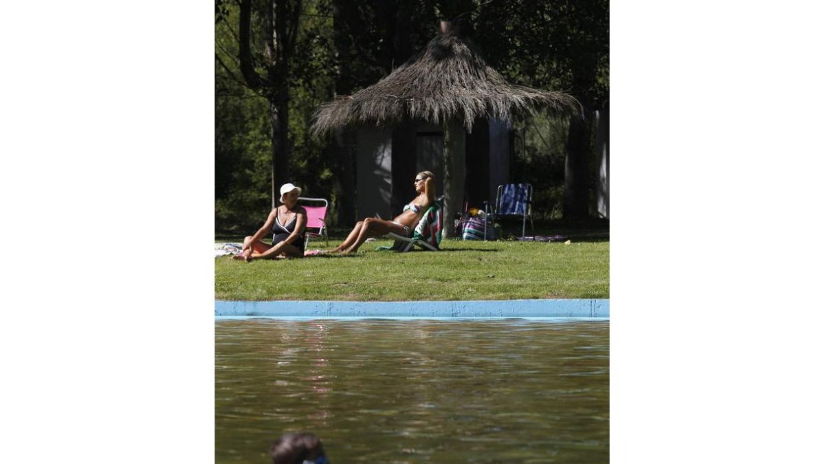 Dos mujeres toman el sol mientras un niño se da un chapuzón en la playa fluvial de Quintanilla de Sollamas.