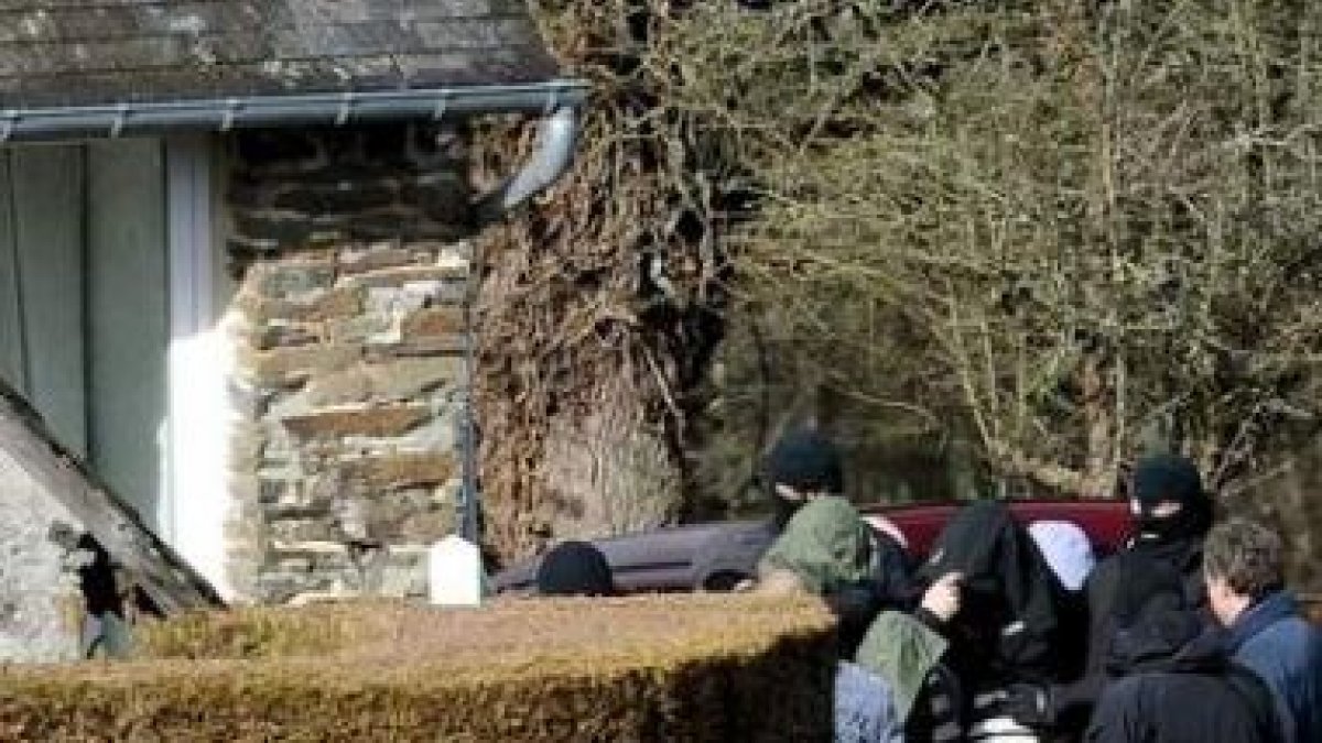 Agentes de la policía inspeccionan la casa rural junto a uno de los tres detenidos.