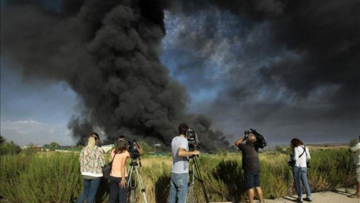 Unos periodistas toman imágenes de la gran columna de humo producida este viernes en un polígono de Chiloeches, Guadalajara.