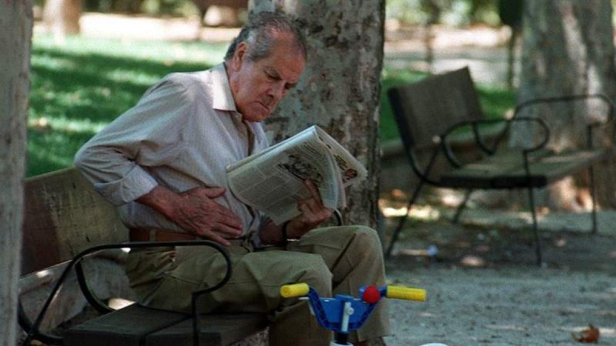 Un abuelo lee el periódico en un parque de Madrid.
