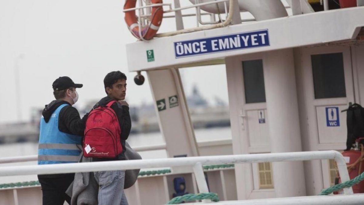 Un migrante pakistaní mira hacia atrás, conducido por un funcionario, en el ferri a punto de partir hacia Turquía, en Lesbos, este viernes.