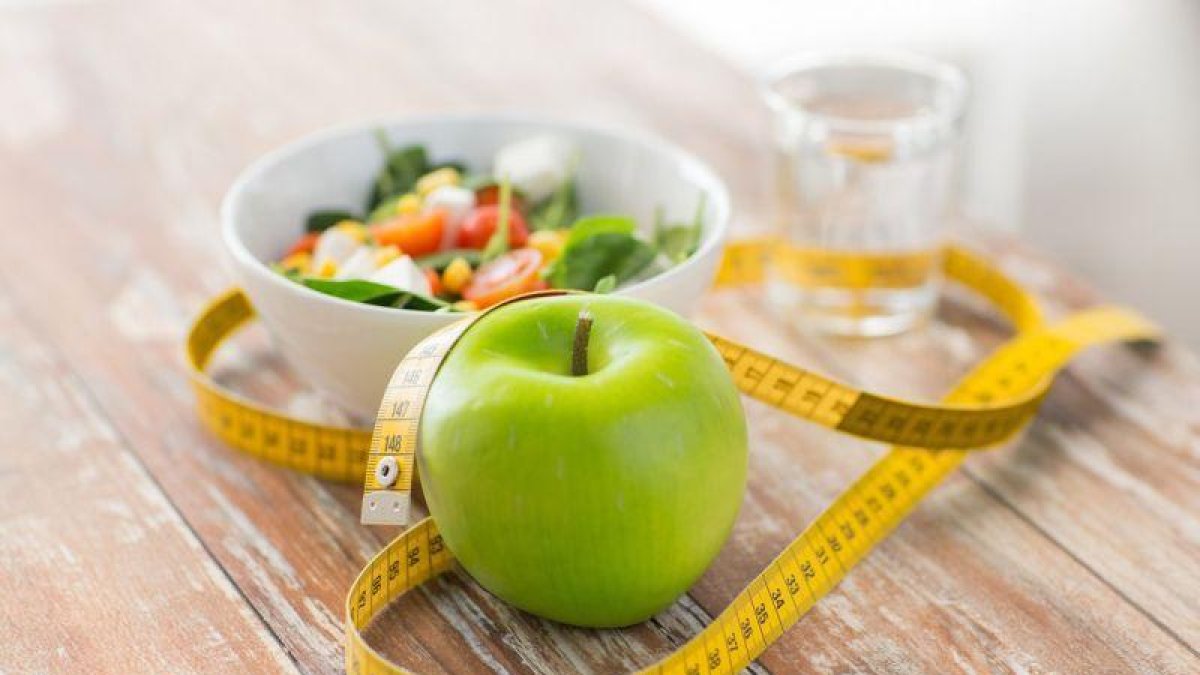Manzana, cinta métrica y desayuno en una mesa.