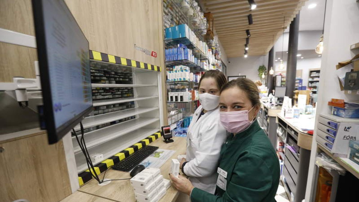 Eva Sánchez y Águeda Anel delante del robot que organiza los medicamentos en la botica.