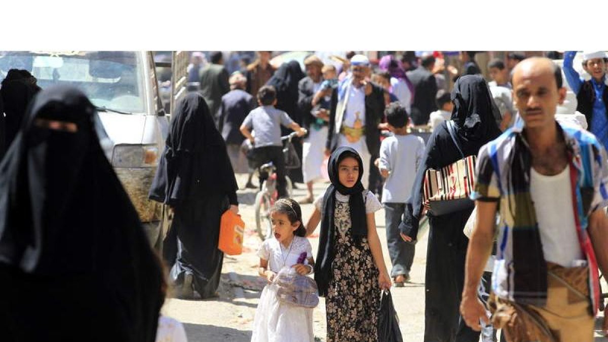 Dos niñas yemeníes pasean entre la gente por un mercado en la ciudad de Sanáa. Abajo, personas afectadas por la guerra hacen cola para recibir sus raciones de comida gratuitas de una organización caritativa local.