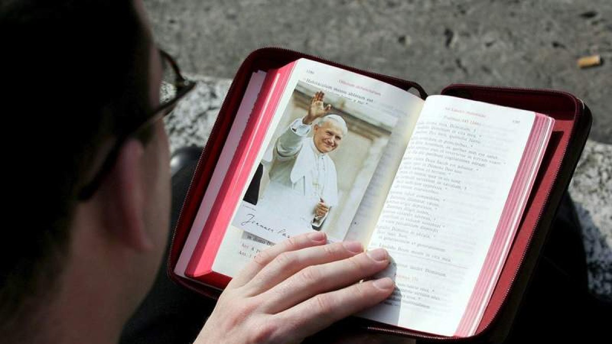 Un sacerdote lee un libro con la imagen del Papa Juan Pablo II como marcador.