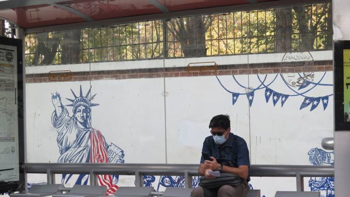 Un iraní espera en la parada de autobús junto a un mural contrario a Estados Unidos. MARINA VILLÉN
