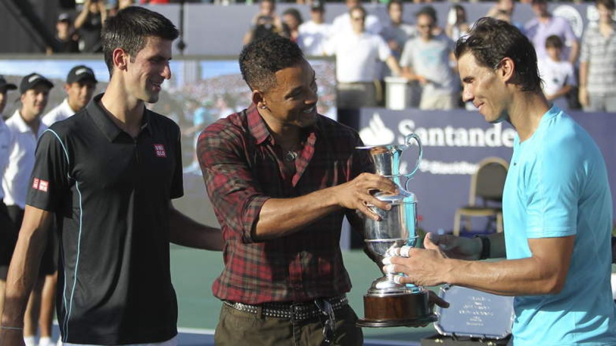 Nadal recibe de Will Smith, con Djokovic de espectador, el trofeo como ganador del partido.