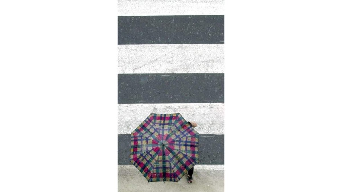 Un viandante cruza un paso de cebra bajo una tormenta.