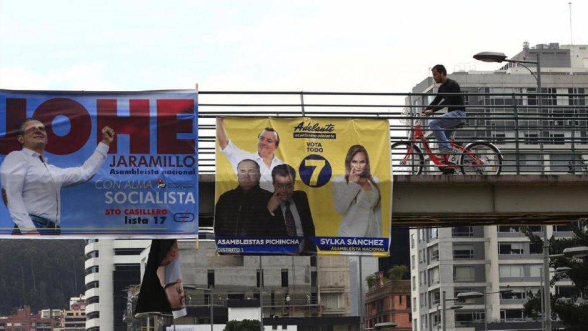 Ciudadanos caminan frente a varios carteles electorales en Quito.