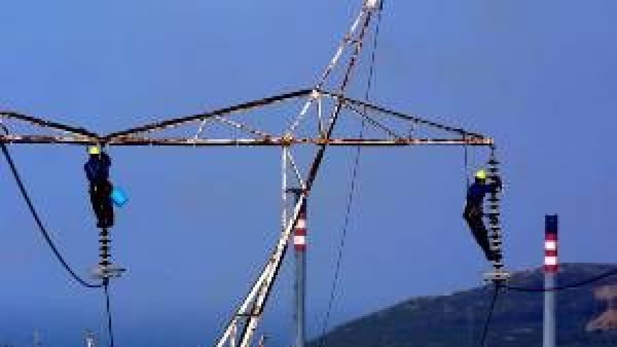 Dos operarios, sujetos por arneses, intentan reparar una línea eléctrica