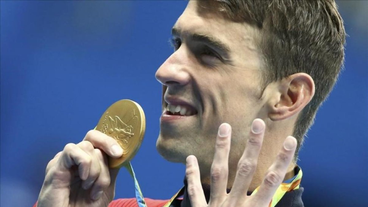 Phelps muestra su medalla señalando los cuatro oros que ha conseguido hasta ahora.