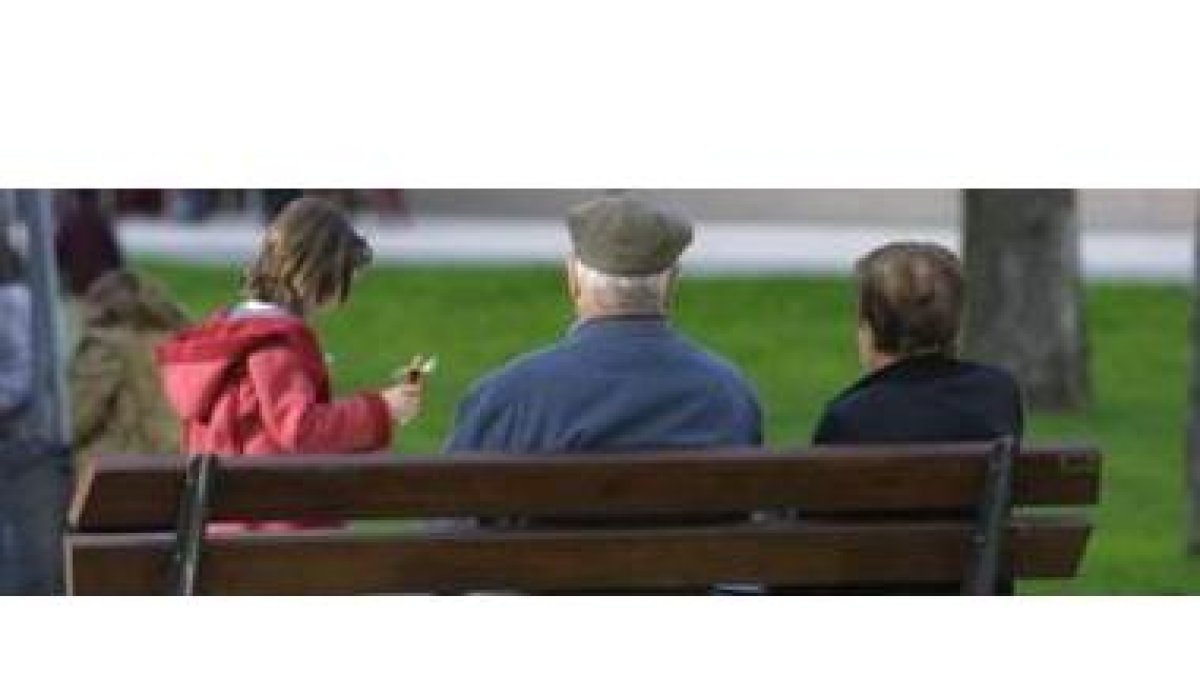 Una pareja de personas mayores observa a una niña que juega en un parque de León.