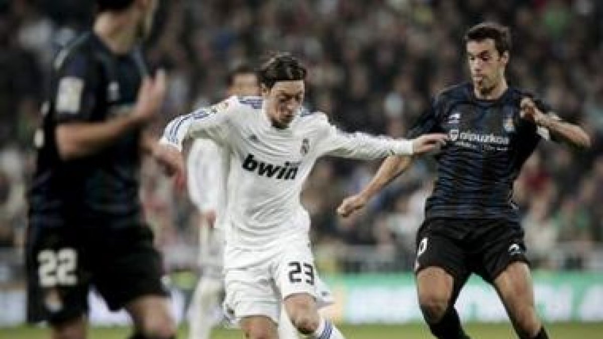 Özil conduce el balón entre los jugadores de la Real Sociedad Xabi Prieto y Daniel Estrada.