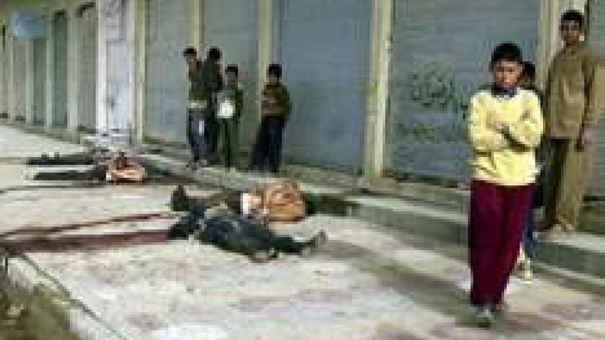 Un grupo de niños mira en Ramadi los cuerpos de varios iraquíes asesinados por los rebeldes