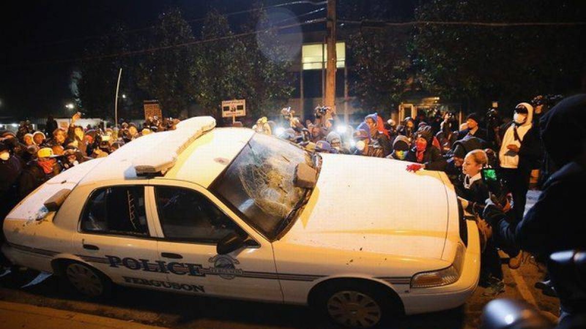 Vecinos de Ferguson golpean un coche de policía, el martes durante las protestas.