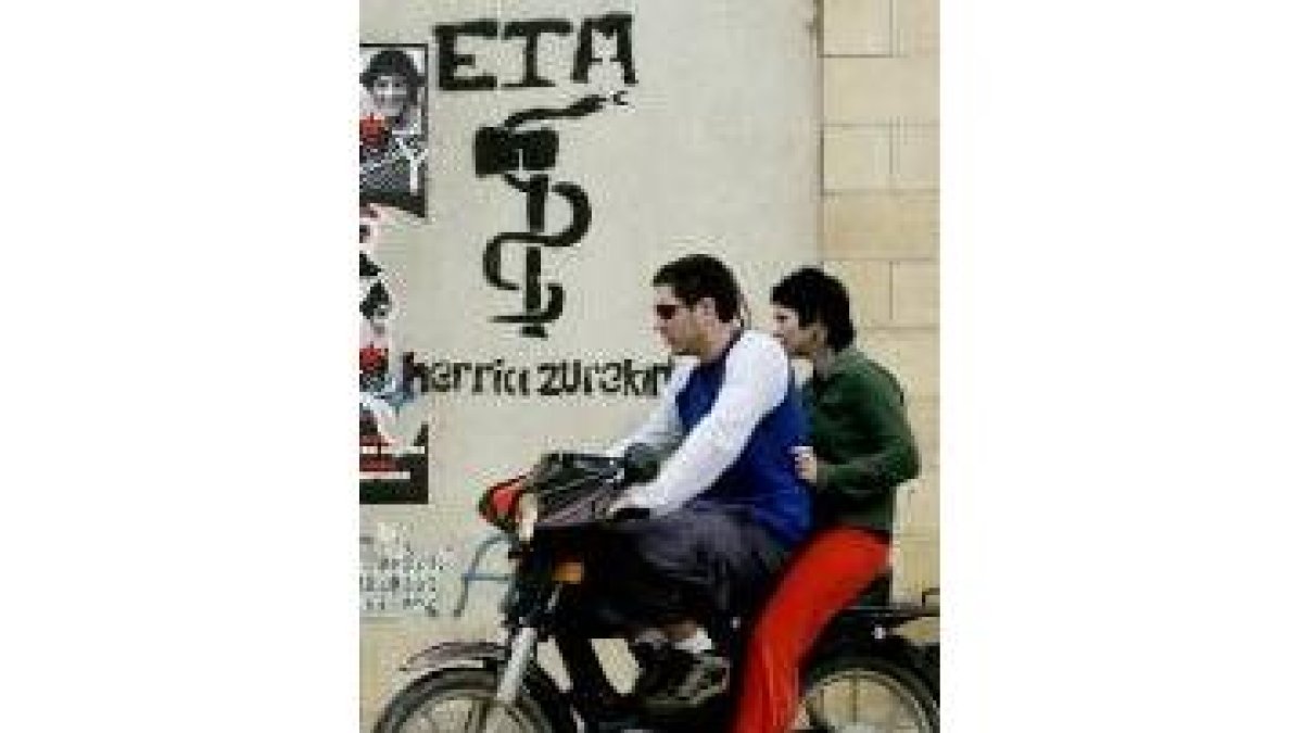 Unos jóvenes conducen una moto delante de una pintada de ETA