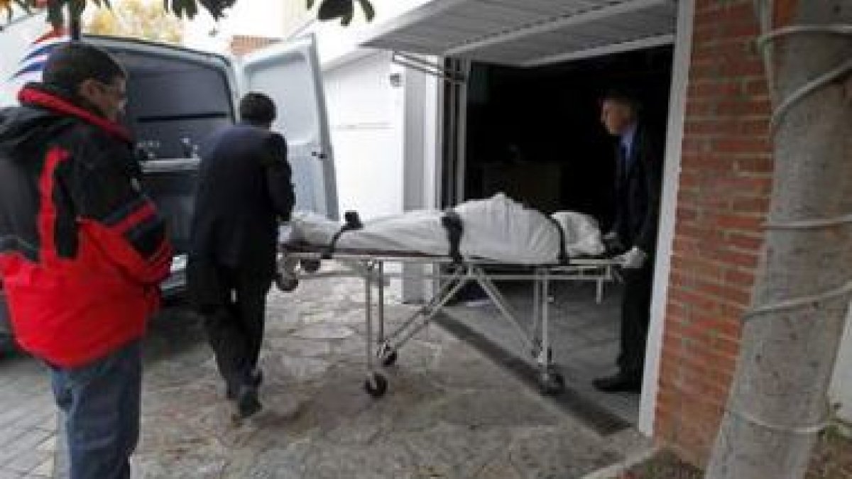 Los servicios funerarios trasladan a un vehículo el cuerpo de una de las víctimas.