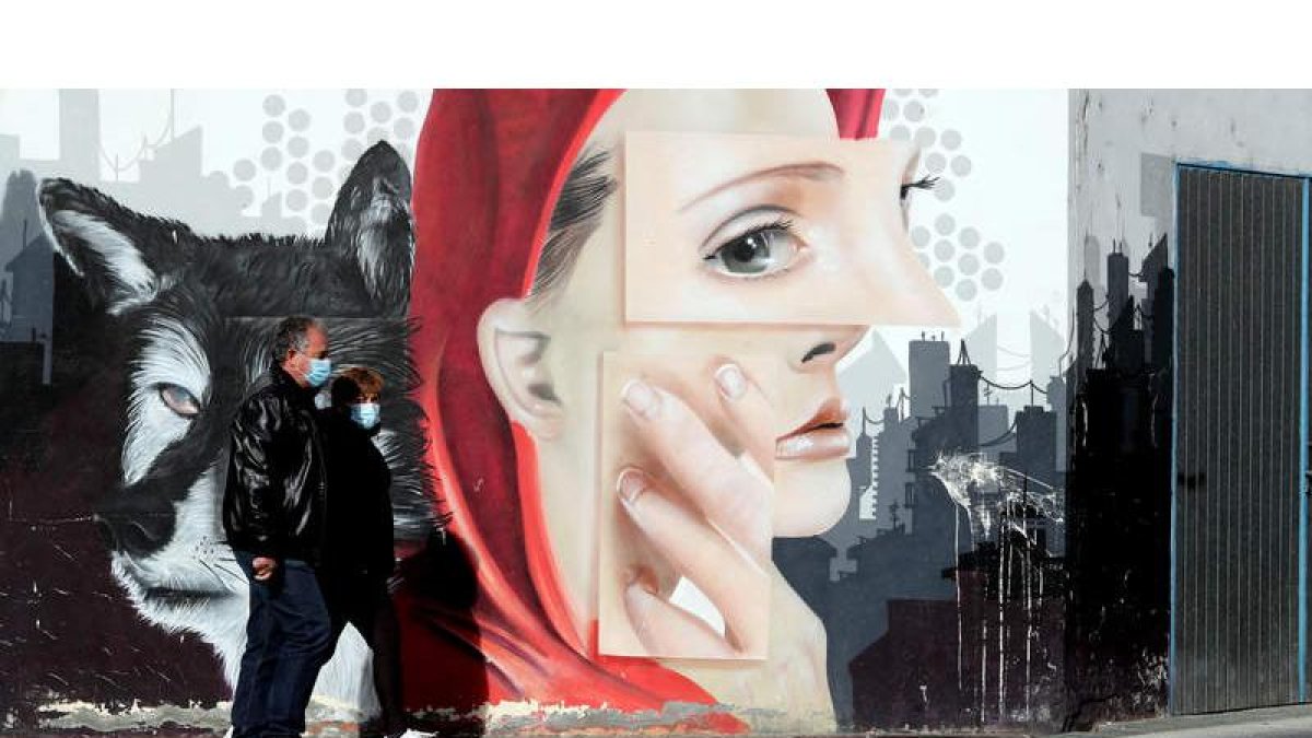 Una pareja, ayer por la mañana caminando por una calle de Ponferrada frente a un grafiti en el día del confinamiento perimetral. ANA F. BARREDO