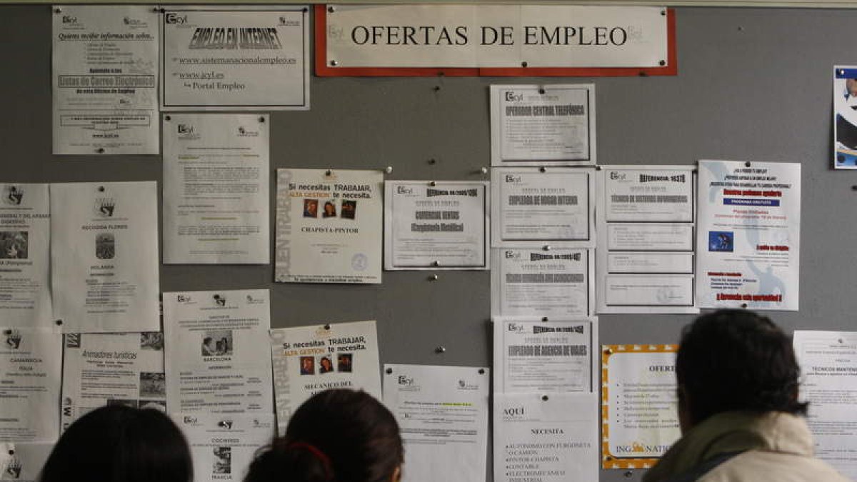 Unos parados consultan ofertas de empleo en una oficina.