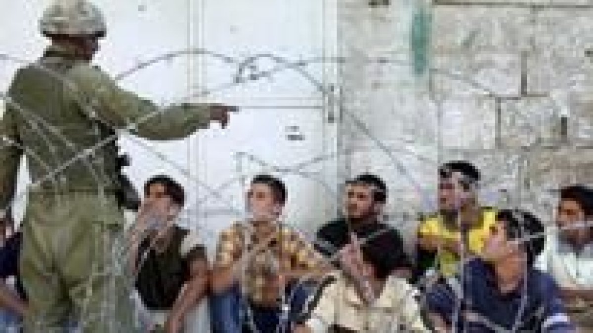 Un soldado israelí vigila a varios palestinos, detenidos ayer en la ciudad cisjordana de Hebrón