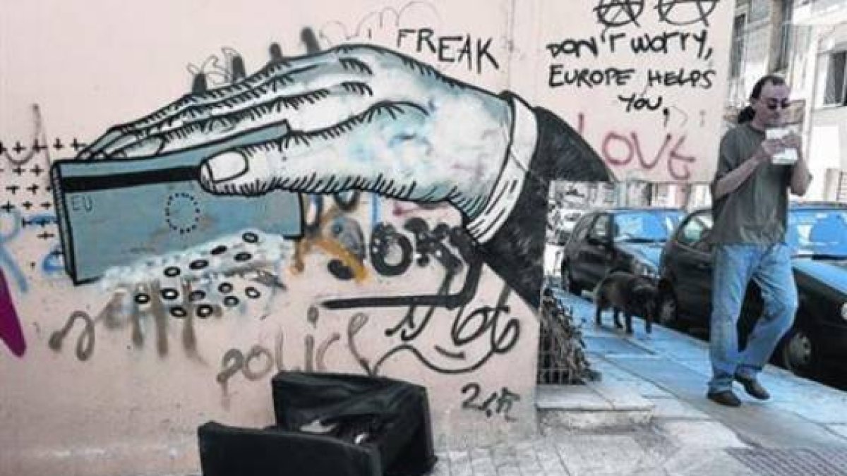 Un hombre pasa ante un grafiti de denuncia en la ciudad de Atenas, este lunes.